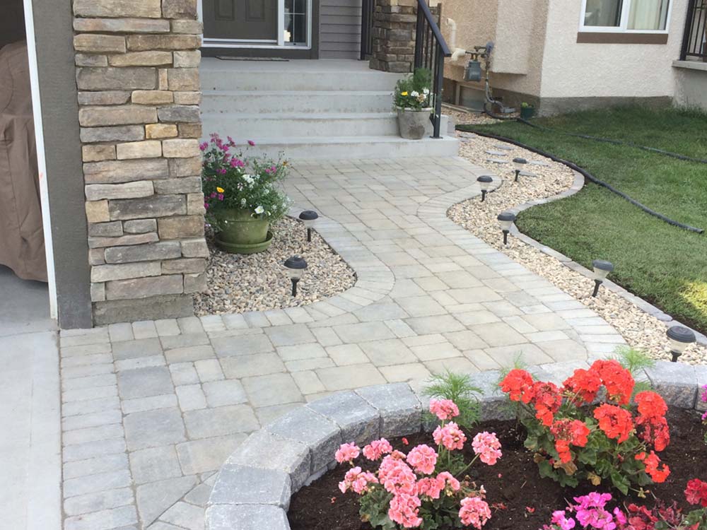 custom stone interlock pathway with gravel gutters and a large stone planter at the edge of a backyard lawn