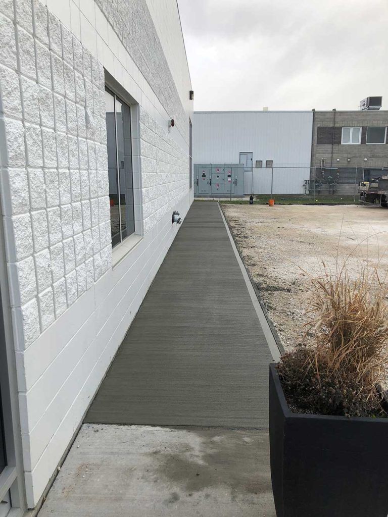 a long concrete walkway by the side of a white stone commercial building