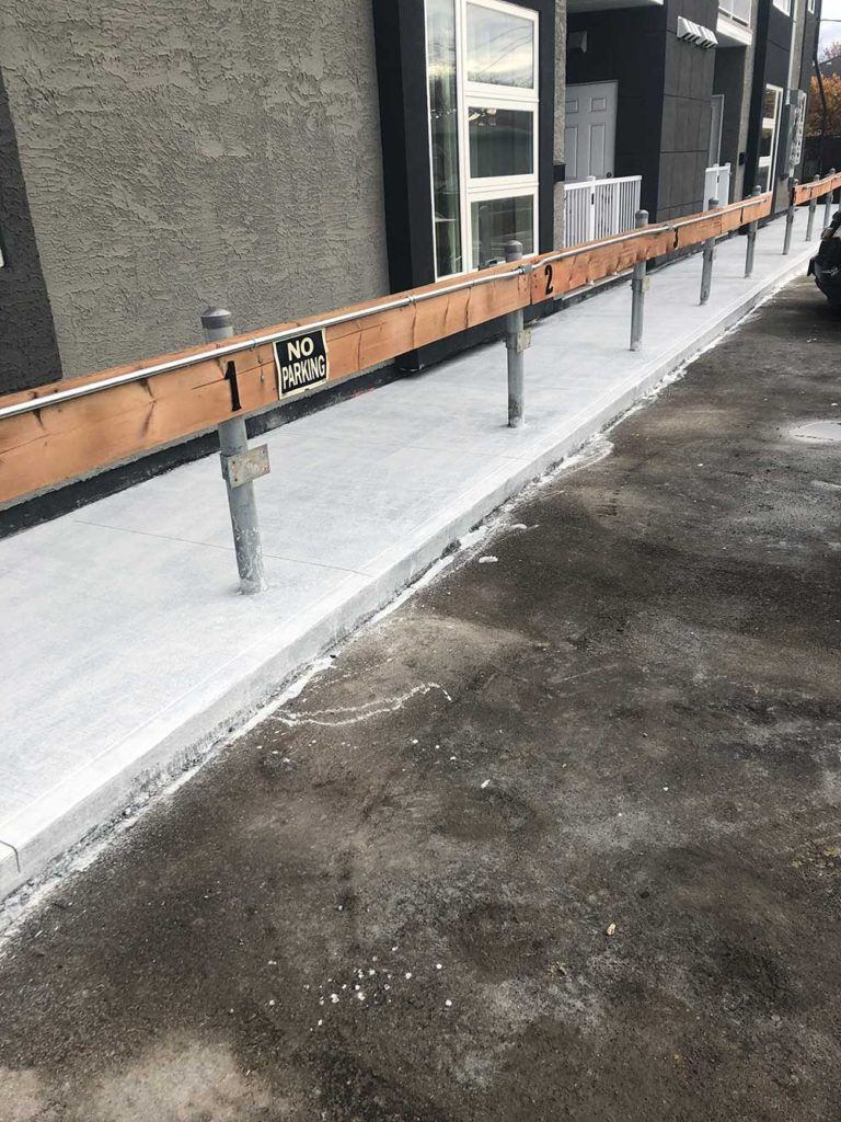 a newly poured concrete walkway at the edge of a lot of numbered parking spaces